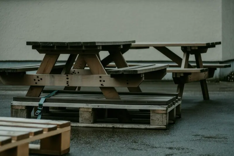 Folded trestle tables and stacked wooden benches strapped to a pallet in a yard, ready for collection.