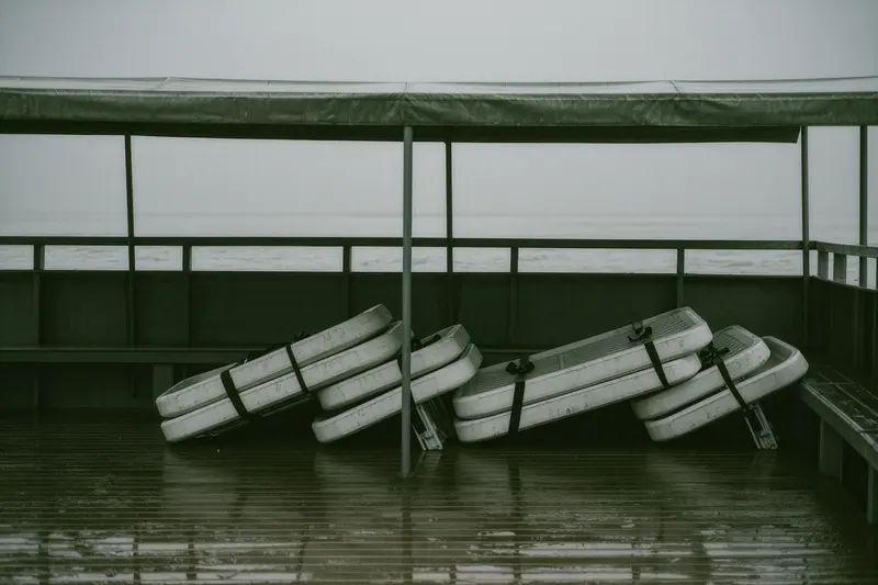 The empty upper deck of a small river vessel, folded chairs stacked against the rail and a bare deck surface under grey sky.